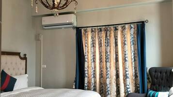 A hotel room with a bed, a chair, a chandelier, and a window with curtains.