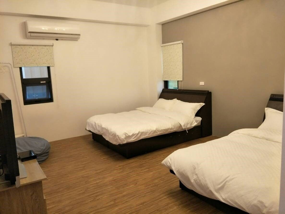Une chambre d’hôtel avec deux lits, un plancher en bois, un climatiseur et une petite fenêtre avec un rideau.