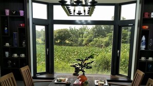 Un comedor con una mesa grande dispuesta para cuatro personas, rodeada de sillas, y vista a un jardín exuberante a través de un ventanal.