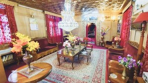 A traditional room with a wooden ceiling, red curtains, a chandelier, and a central table with floral arrangements. - Lake Victoria Houseboat (Srinagar)