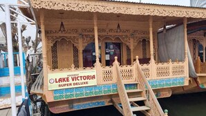 A houseboat named 'Lake Victoria Super Deluxe' with ornate wooden railings and a ladder leading to the entrance. - Lake Victoria Houseboat (Srinagar)