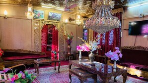 A traditional room with ornate chandeliers, red curtains, and a large flat-screen TV. - Lake Victoria Houseboat (Srinagar)