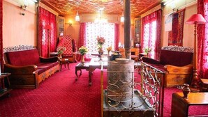 A traditional room with a patterned ceiling, red curtains, and a central wooden column. - Lake Victoria Houseboat (Srinagar)