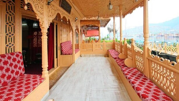 A corridor with ornate wooden railings and benches, leading to a balcony with a view of a cityscape. - Lake Victoria Houseboat (Srinagar)