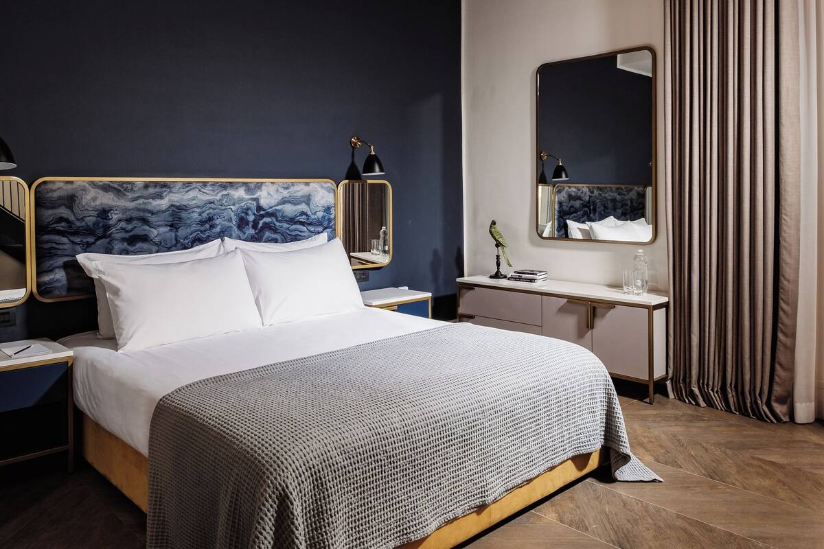 Camera da letto moderna con un letto grande, comodini, un tavolino, una lampada da comodino, uno specchio e una finestra con tende.