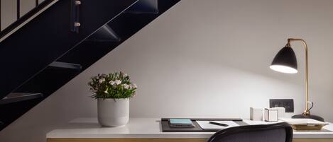 A modern office space with a desk, a chair, a potted plant, a lamp, and a staircase.