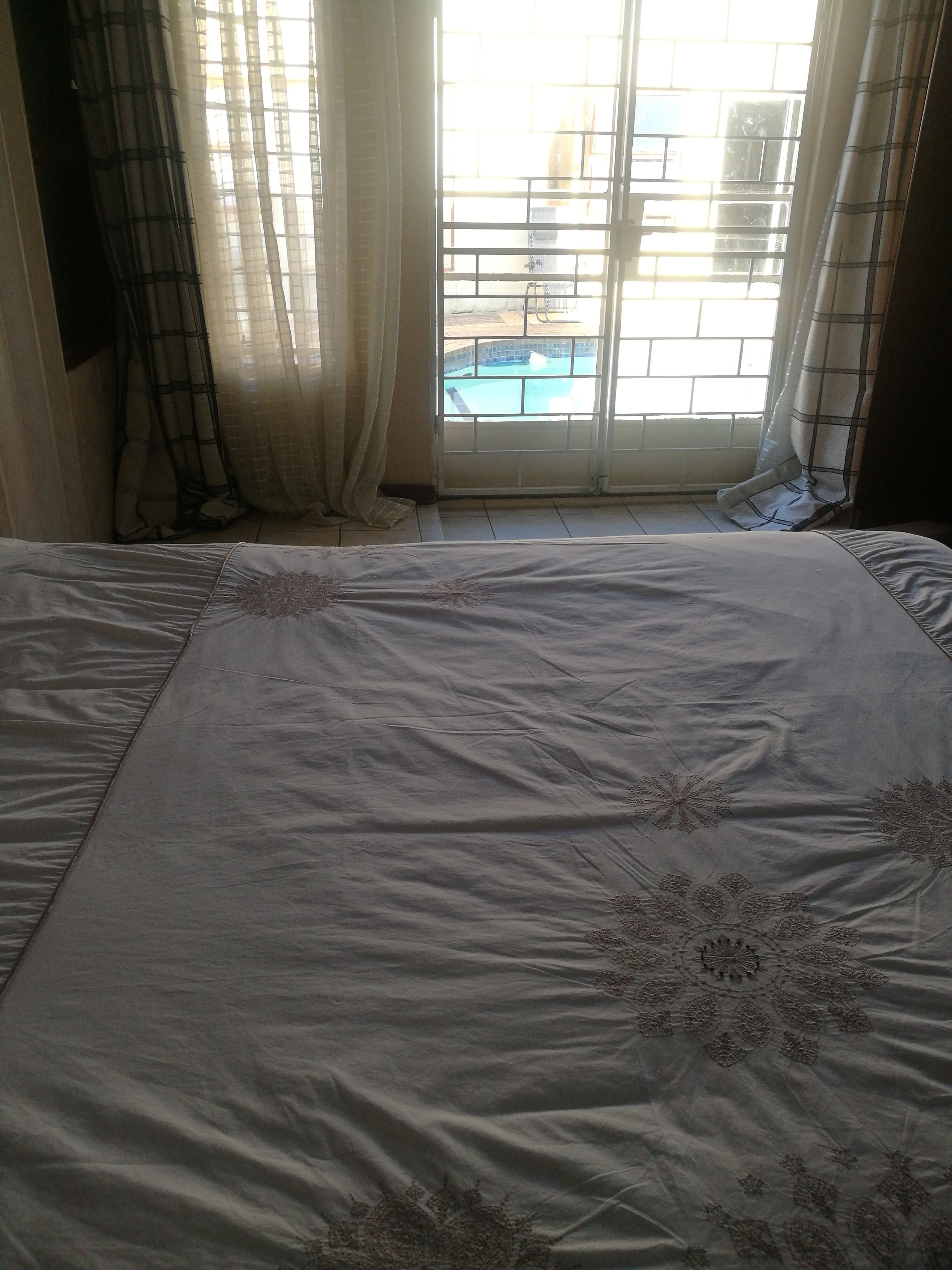 A bedroom with a large bed, a window with a view of a swimming pool, and sheer curtains.