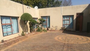 Une cour avec un chemin en briques, des plantes en pot et un petit arbre.