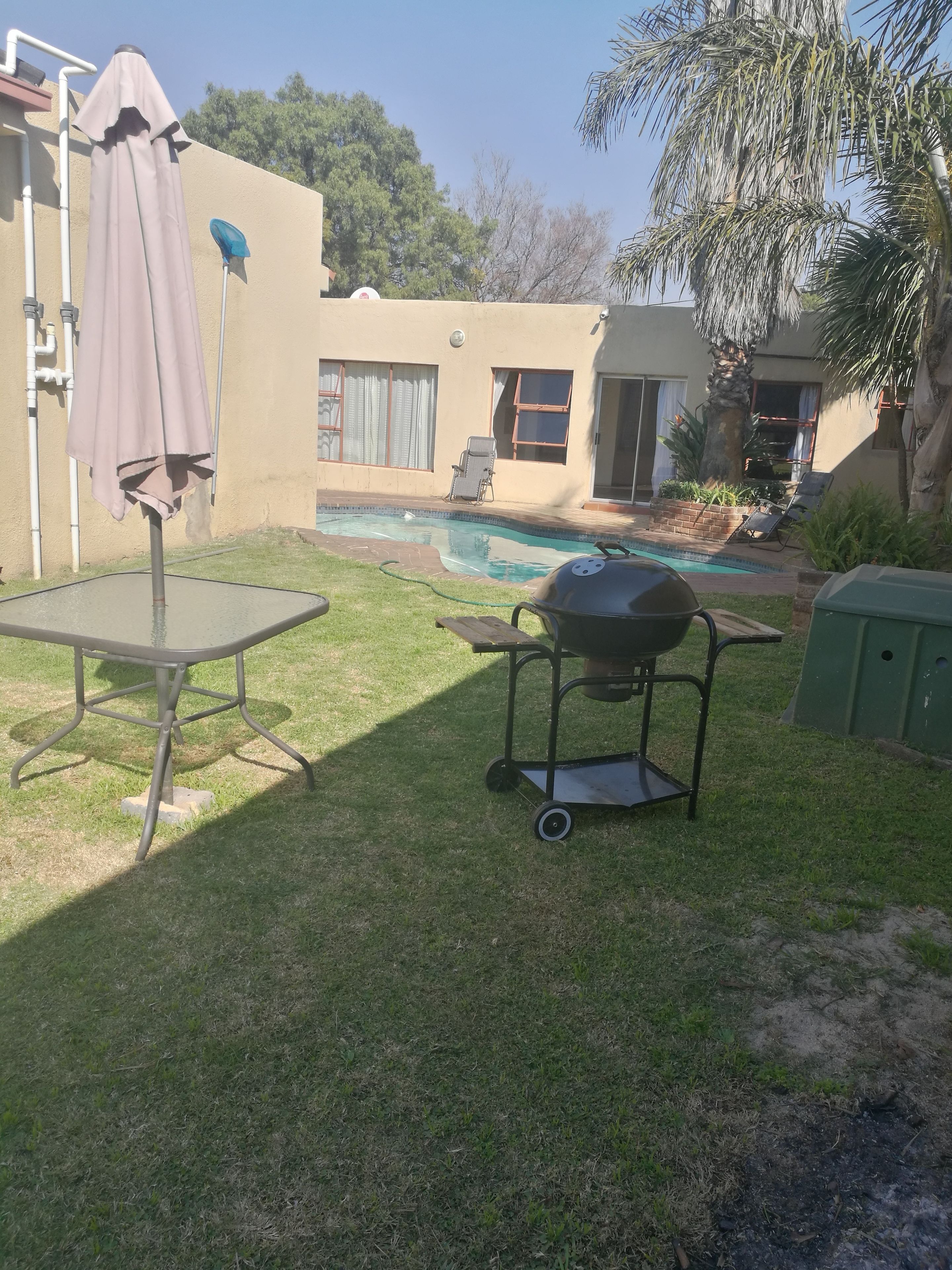 Un patio trasero con piscina, parrilla y mesa con sombrilla.