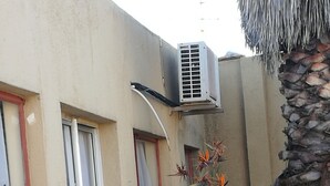 Un bâtiment doté d’une terrasse carrelée, d’un palmier et d’une fenêtre à cadre rouge.