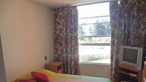 A bedroom with a bed, a TV on a stand, and a window with curtains. - Depto Algarrobo Condominio Regata 1032 (Algarrobo)