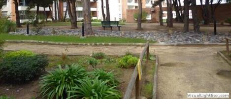 Zona arbolada con un banco y un camino que lleva a un edificio de fachada de ladrillo.