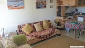 A living room with a patterned sofa, a green armchair, and a dining area with a table and chairs. There is a kitchen area with cabinets and a countertop. - Depto Algarrobo Condominio Regata 1032 (Algarrobo)