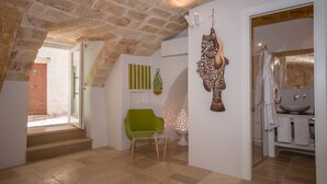 A spacious room with a high ceiling, a green chair, a decorative wall piece, and a bathroom with a sink and towel rack.