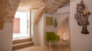 A room with a stone ceiling, a green chair, a glass table, and a wall-mounted decorative piece.