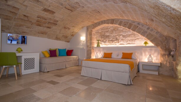 A cozy room with a stone ceiling, a bed with orange bedding, a green chair, and a small table with a lamp.