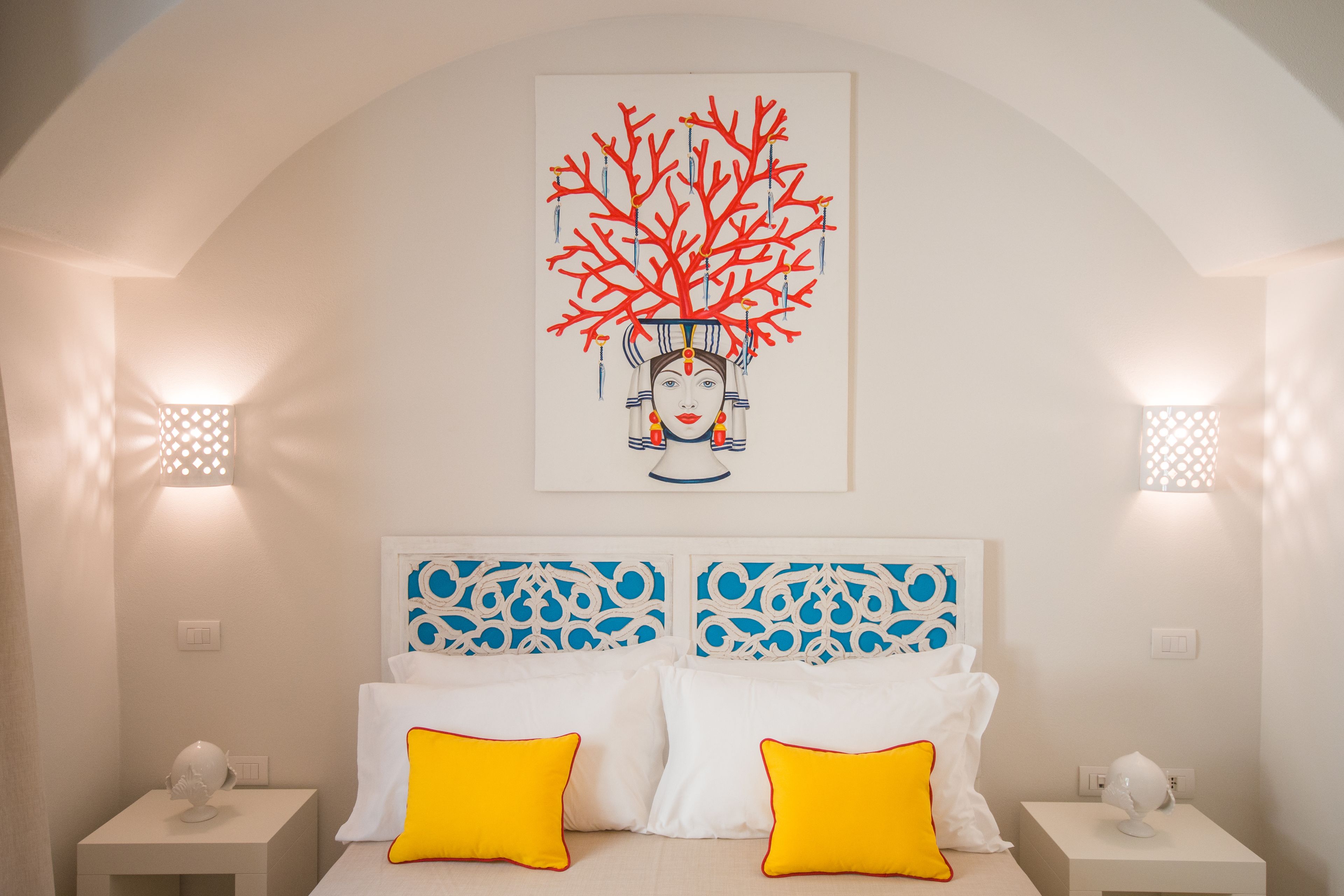 A bedroom with a white bed, two yellow pillows, a decorative headboard, and a wall-mounted artwork of a tree.