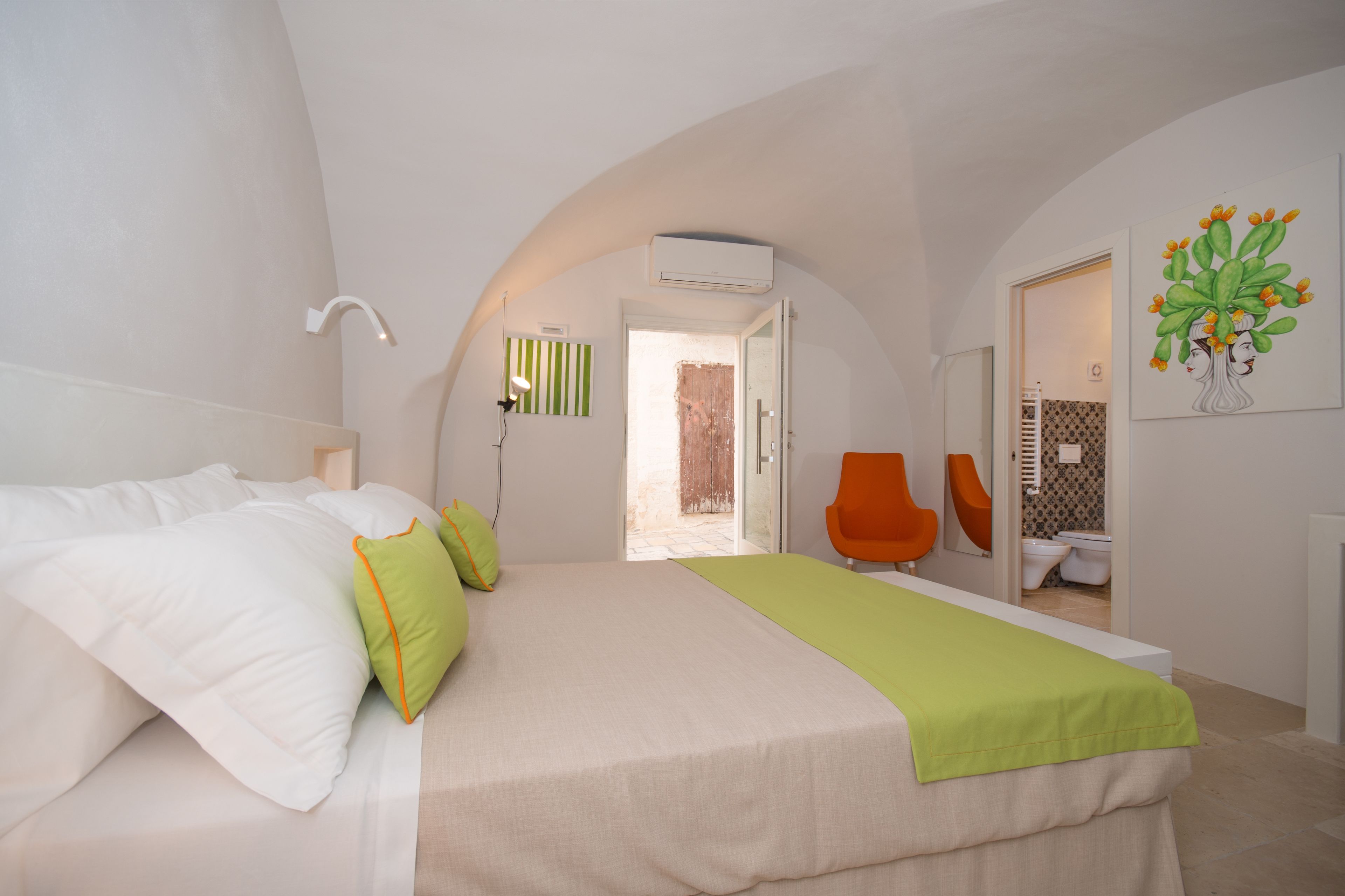 A modern bedroom with a large bed, a green throw, and a view of the bathroom.