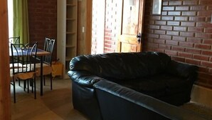 A cozy living room with a black leather sofa, a dining table with chairs, a brick wall, and a wooden ceiling. - Cabaña en Algarrobo 1 El Canelo (Algarrobo)