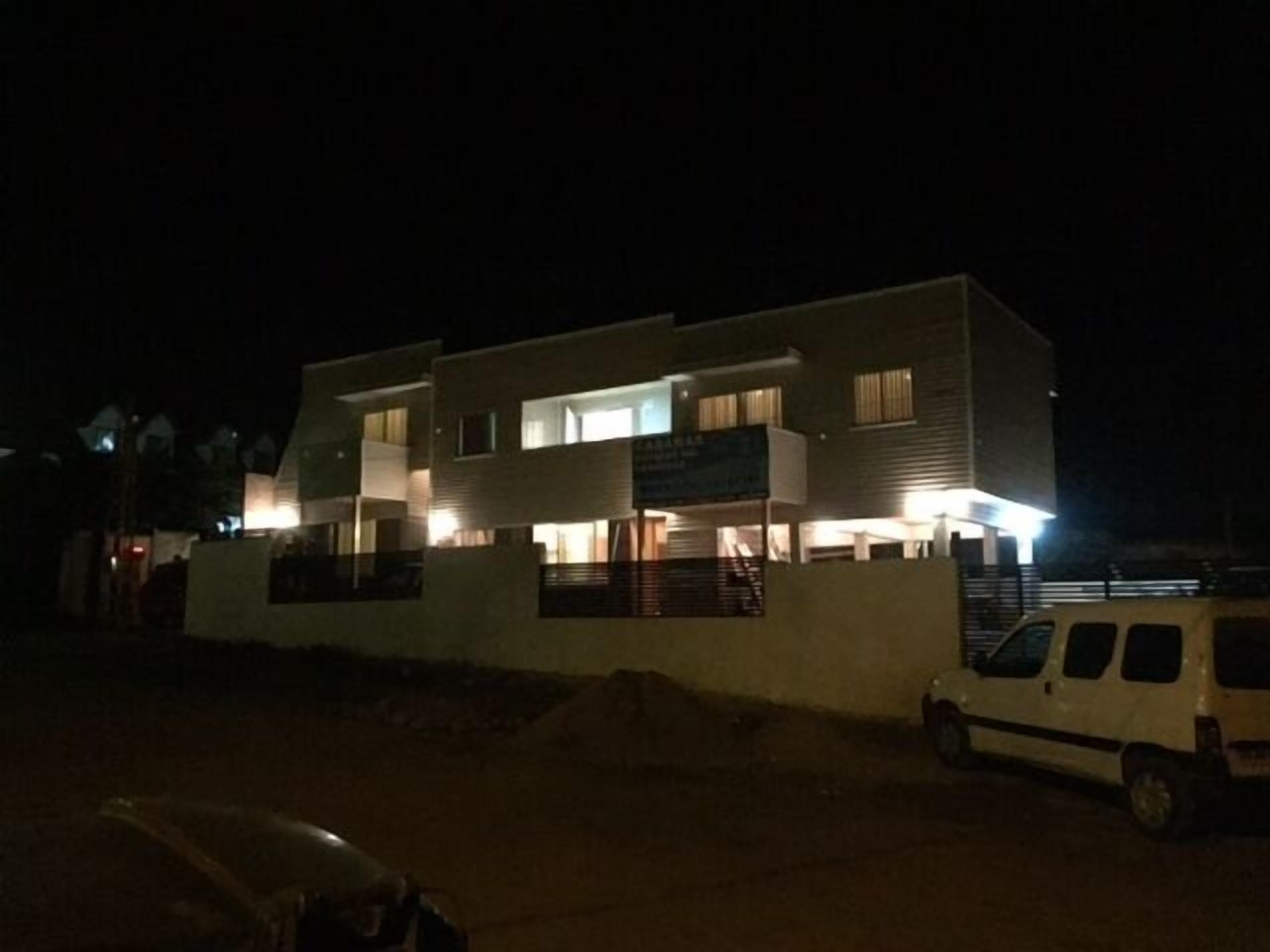 A modern two-story building with multiple illuminated windows and a visible staircase leading to the upper floor.