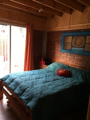 A wooden room with a bed, a brick wall, and a window with curtains. - Cabaña en Algarrobo 1 El Canelo (Algarrobo)