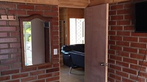 A room with a brick wall, a bed with a blue mattress, a wooden ceiling, and a door leading to another room. - Cabaña en Algarrobo 1 El Canelo (Algarrobo)