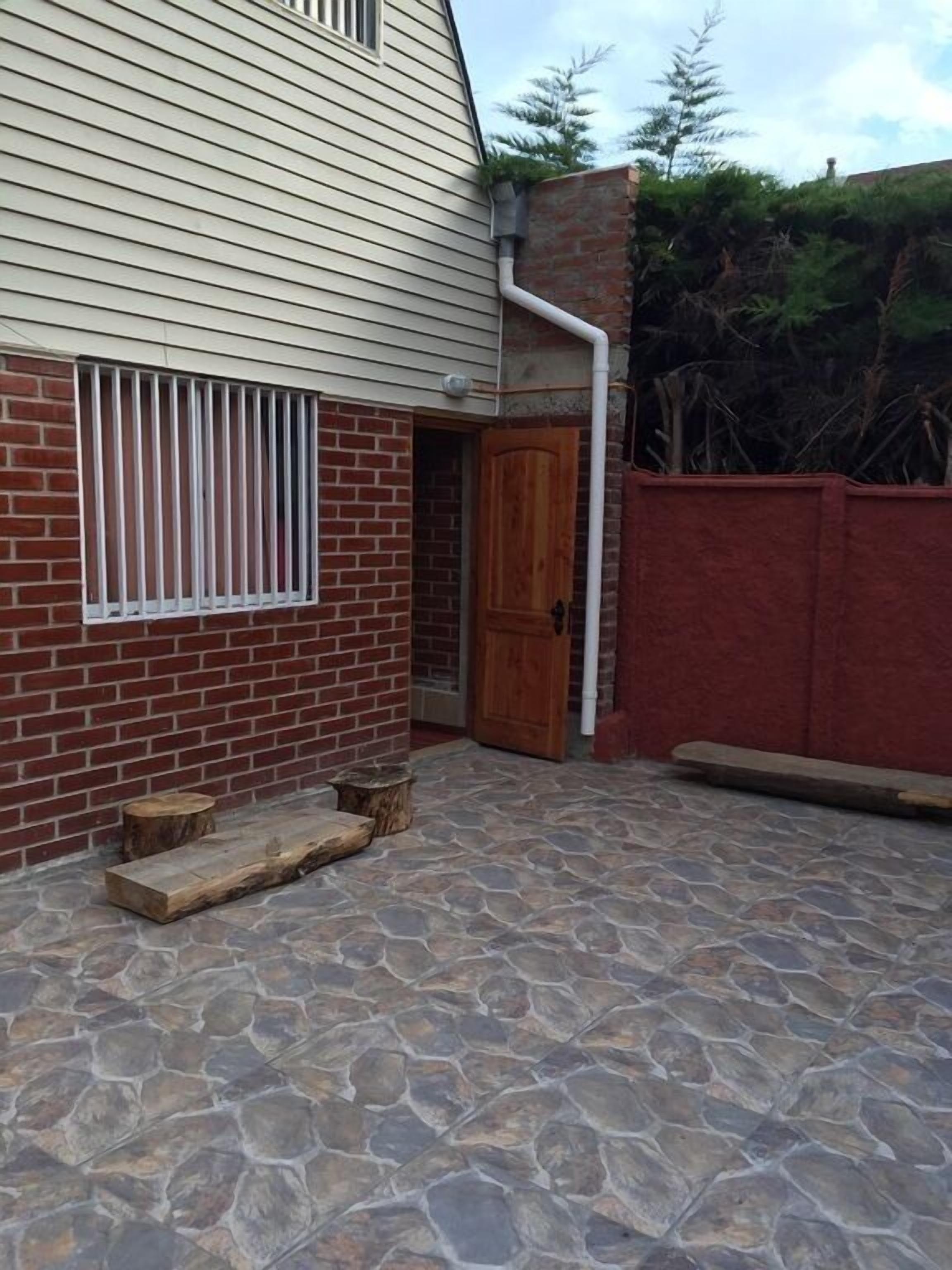 A house with a stone patio, a wooden door, and a window with bars.