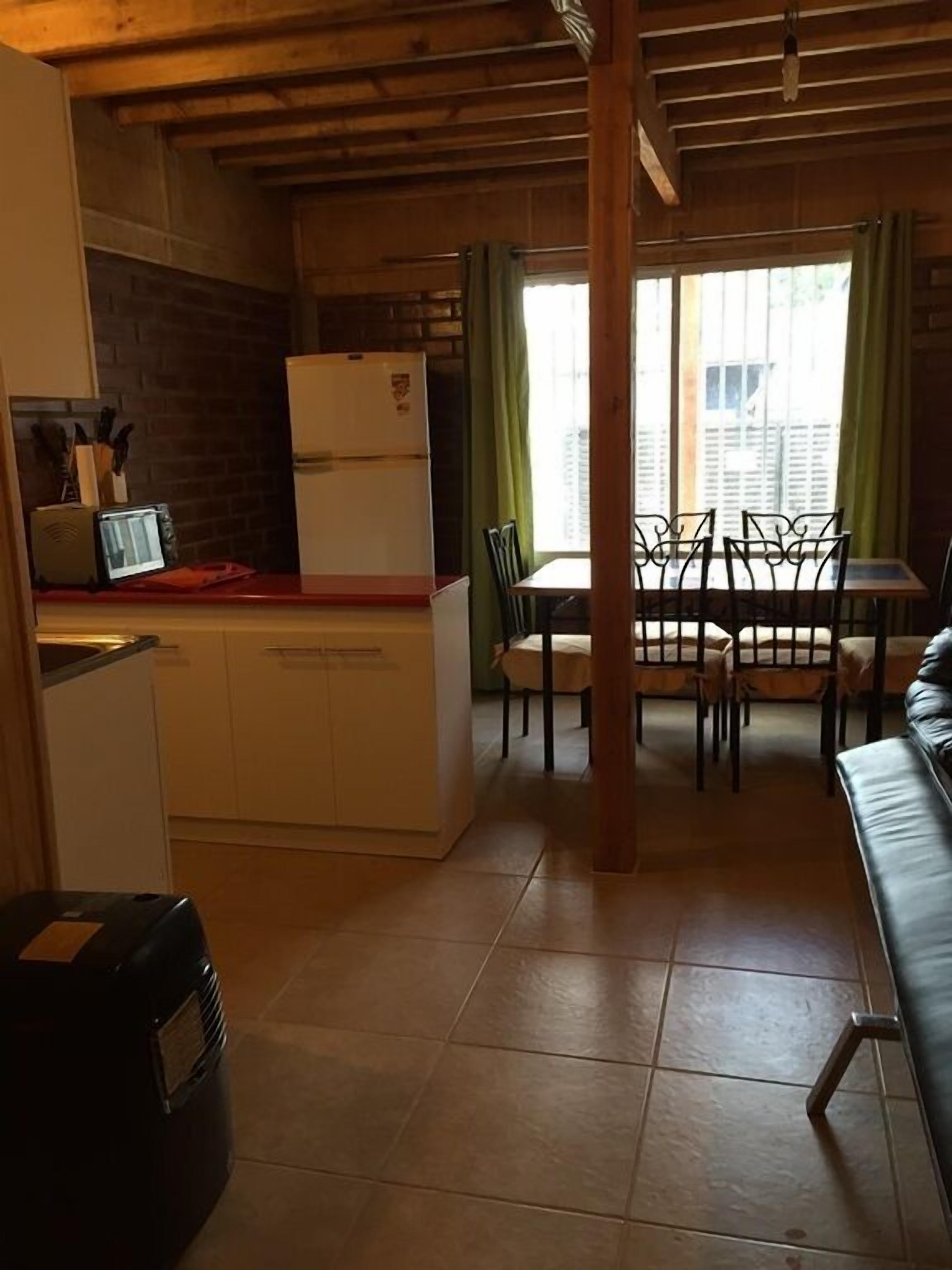 A compact kitchen with a refrigerator, a dining table with chairs, and a wooden ceiling.