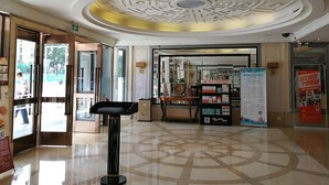 Eine Hotelhalle mit modernem Deckenstil, einer Rezeption und Informationsplakaten.