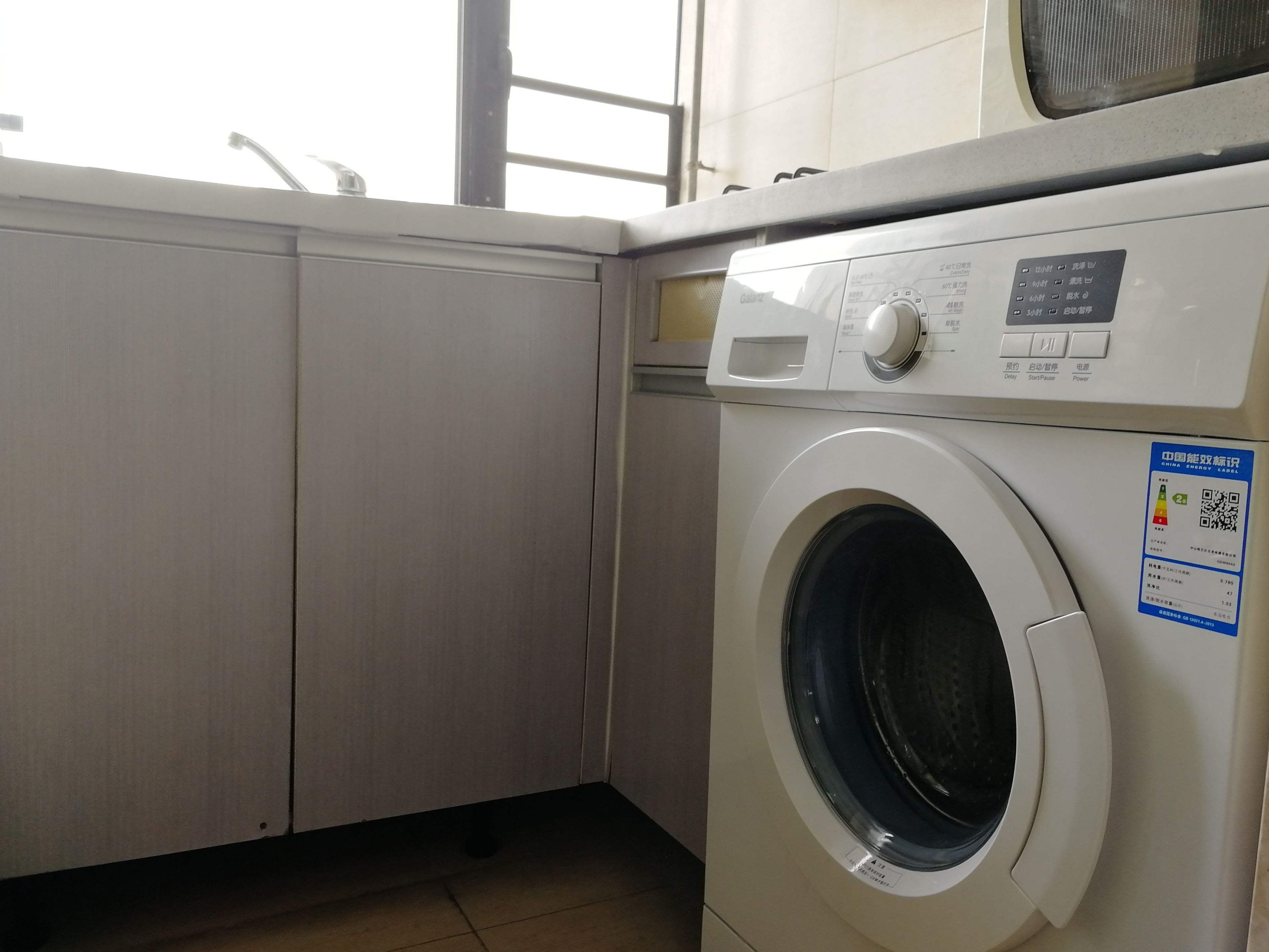 A compact laundry room with a front-loading washing machine, a control panel, and a small window.