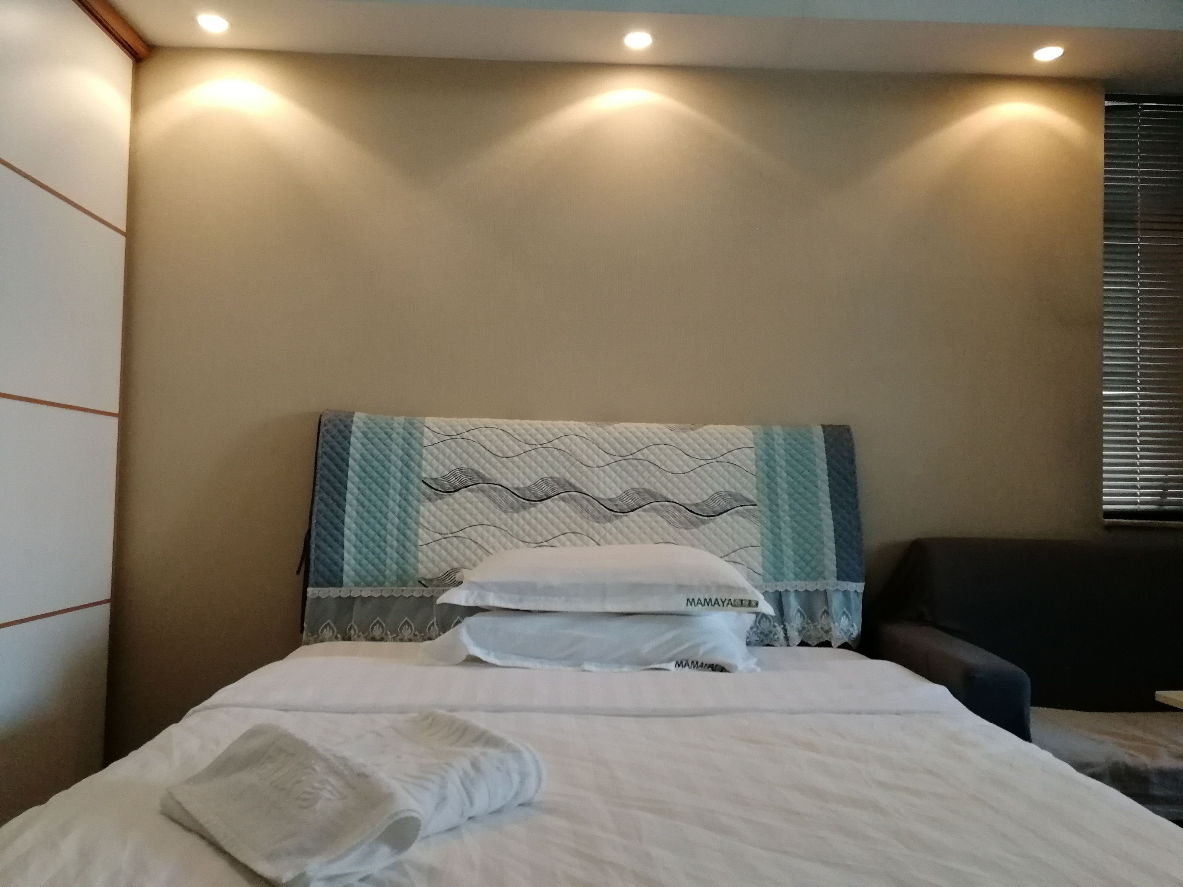 A neatly made bed with a quilted headboard, a pillow, and a folded towel on the bed.