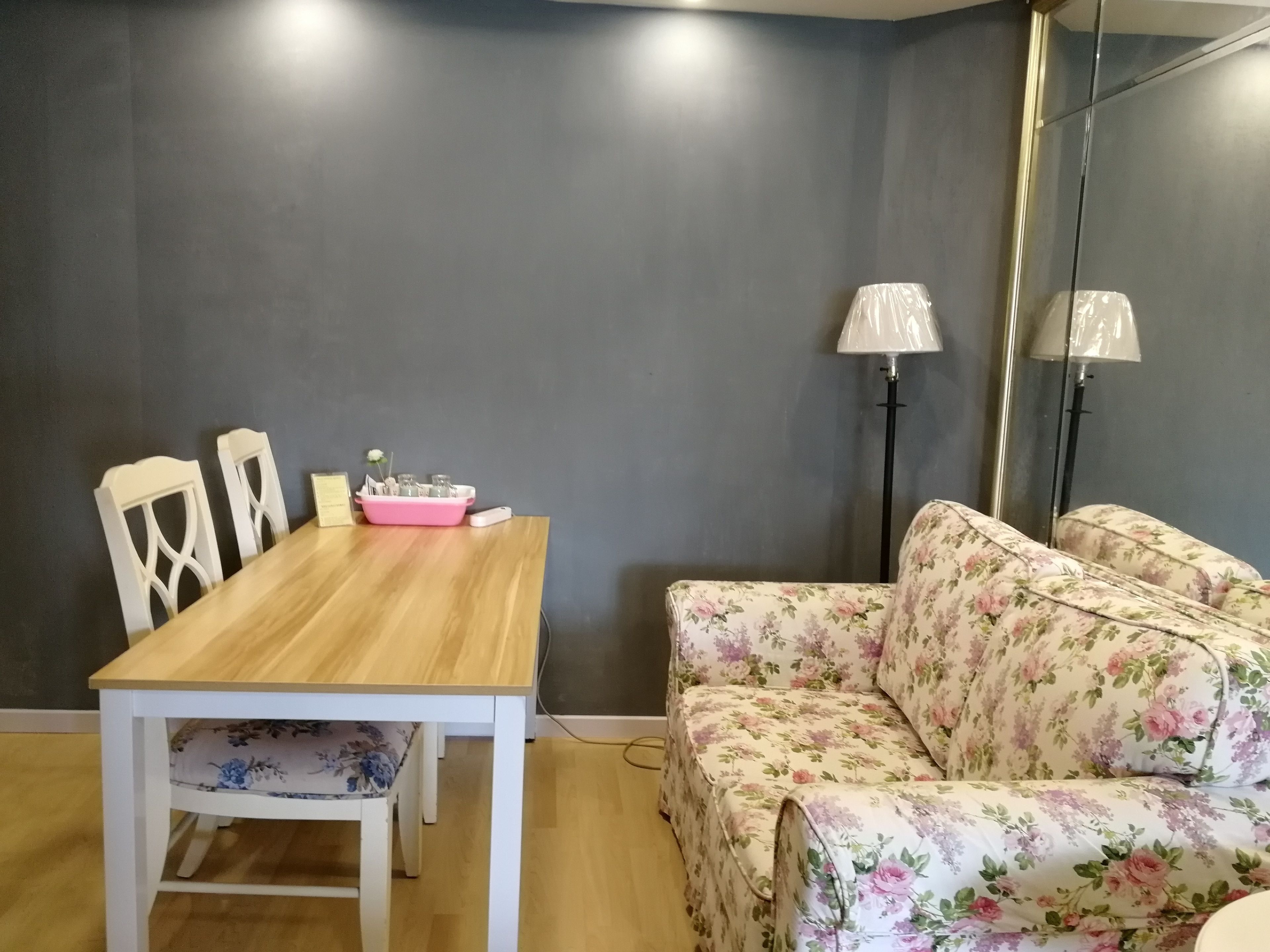 A dining area with a wooden table and chairs, a floral sofa, and two floor lamps.