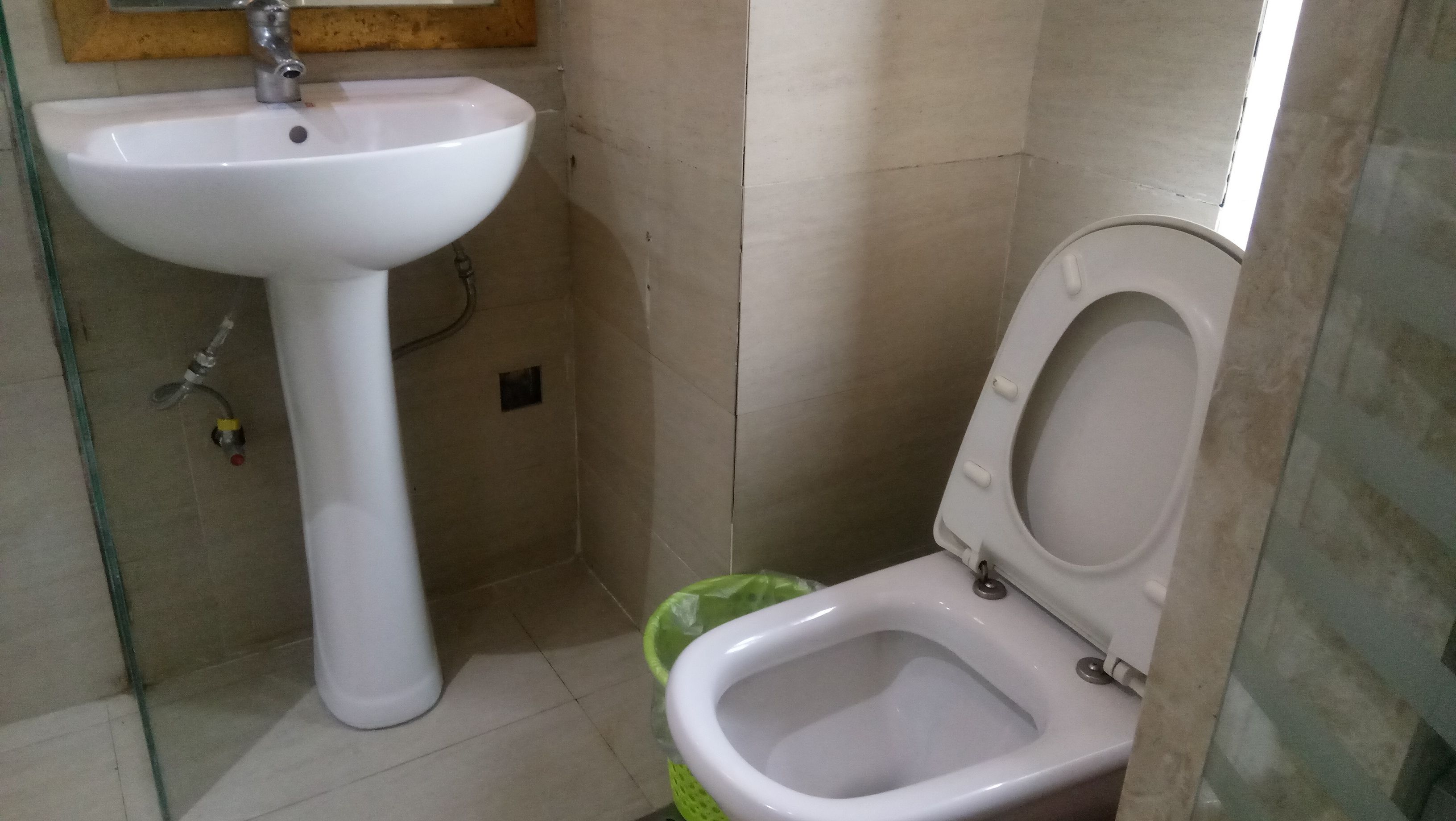 A small bathroom with a pedestal sink, toilet, and a green trash bin.