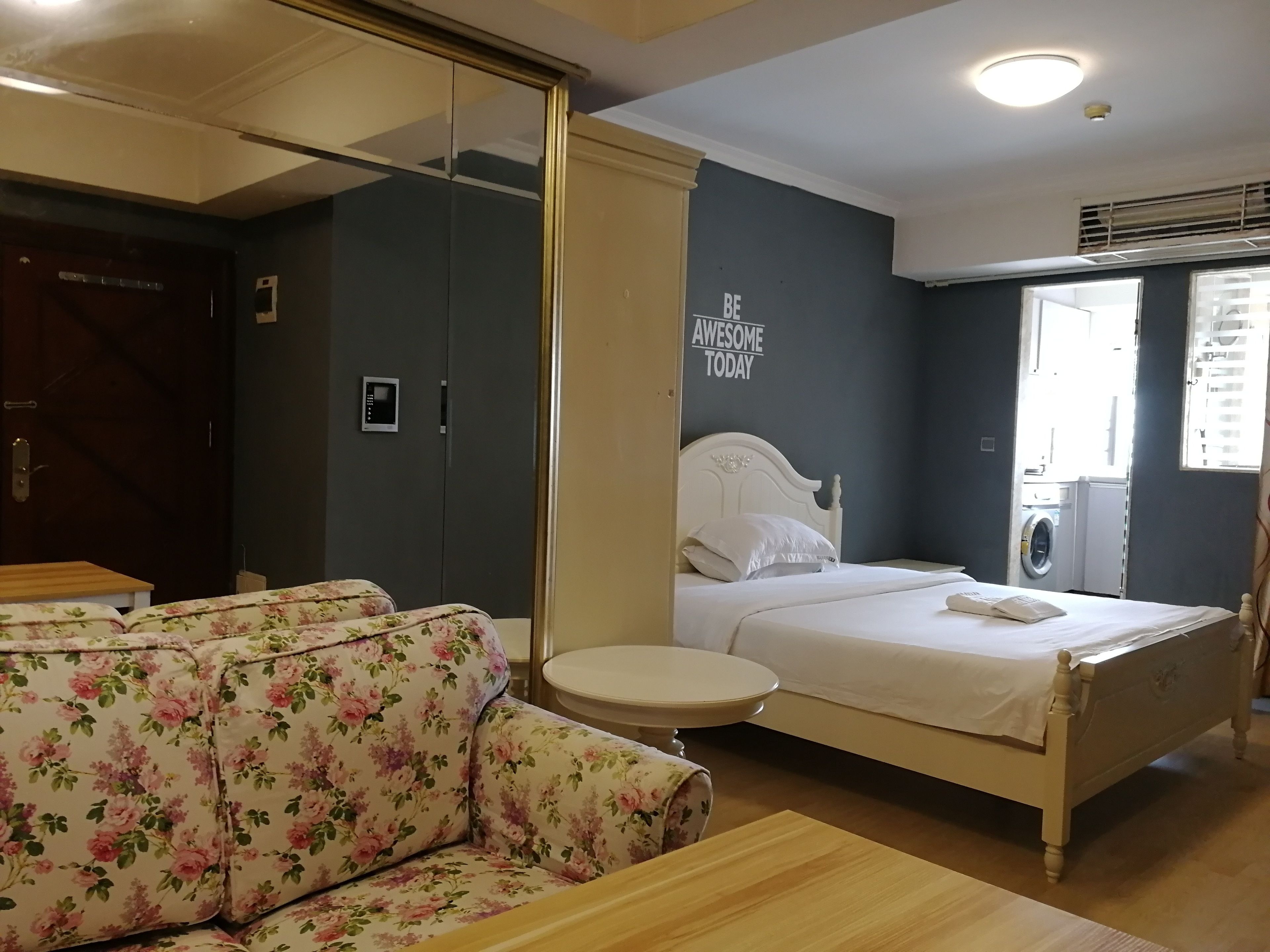A bedroom with a bed, a sofa, a small table, a wardrobe, and a wall with a motivational quote.