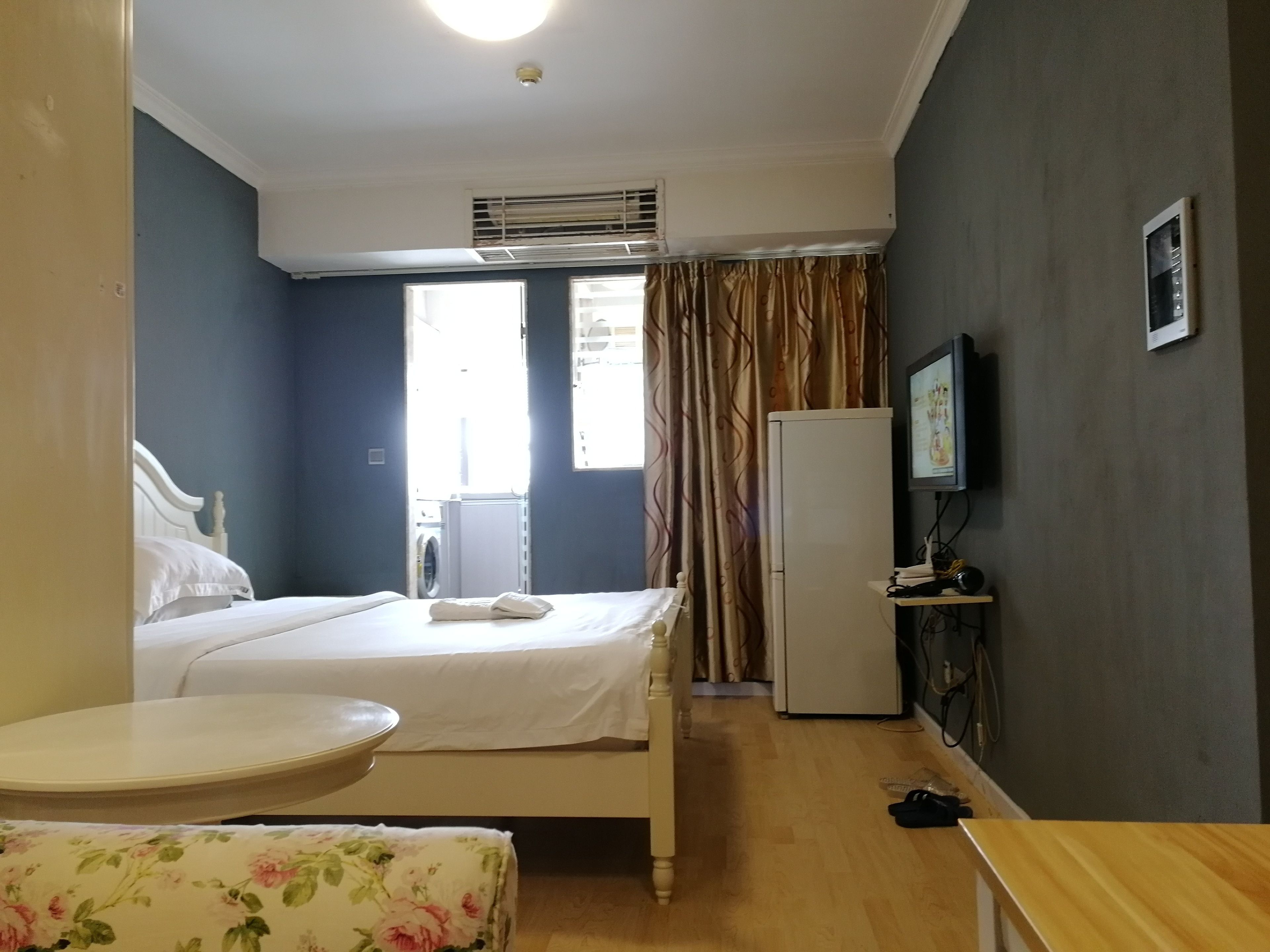A hotel room with a bed, a small table, a washing machine, a refrigerator, and a television.