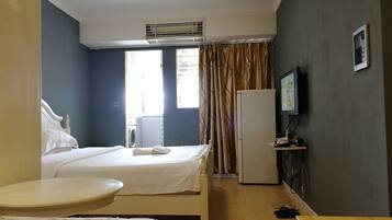 A hotel room with a bed, a small table, a washing machine, a refrigerator, and a television.