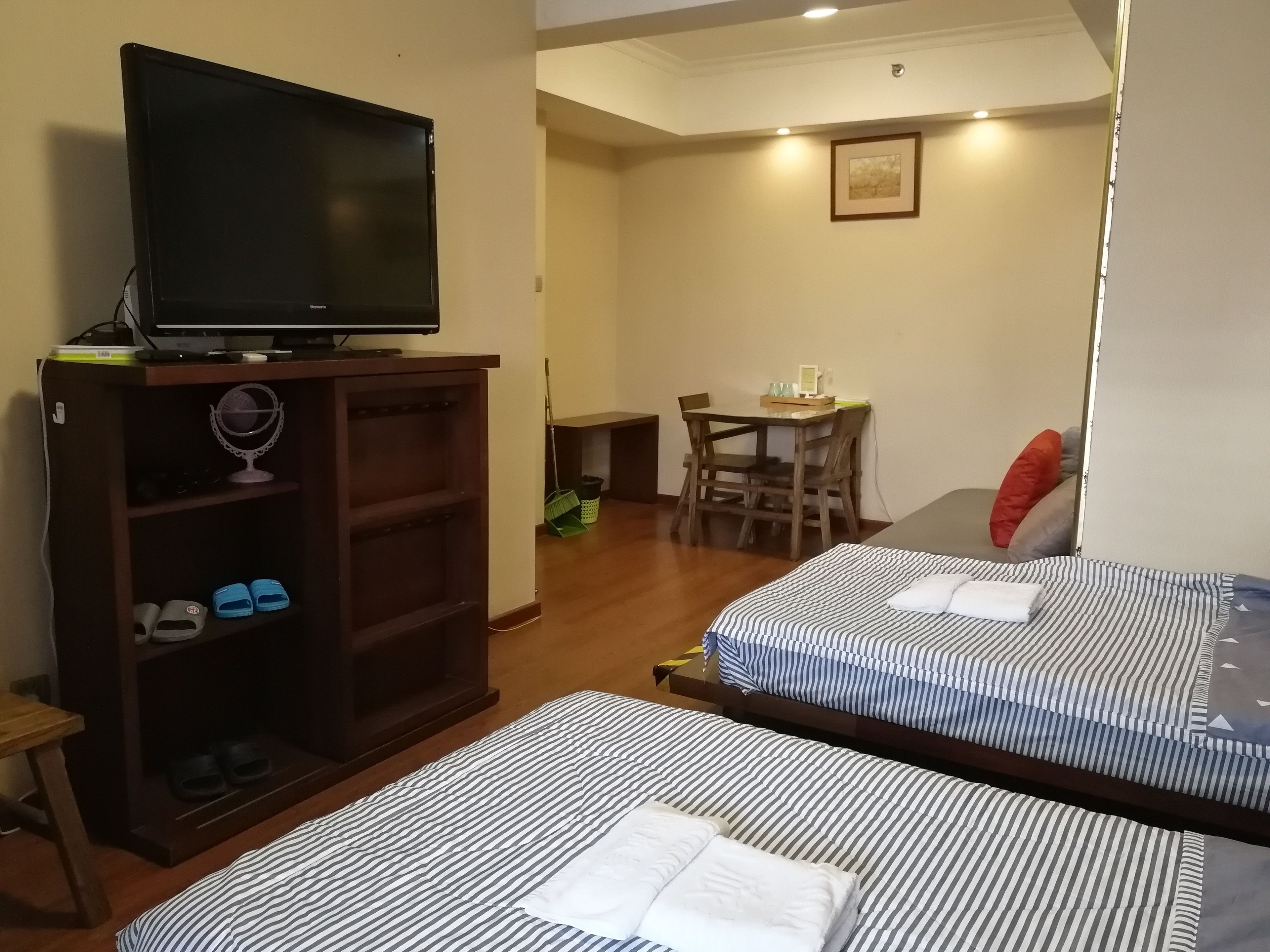A hotel room with two beds, a TV on a stand, a small table with chairs, and a painting on the wall.