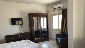 Quarto de hotel com duas camas, um guarda-roupa, uma TV e um ar condicionado.