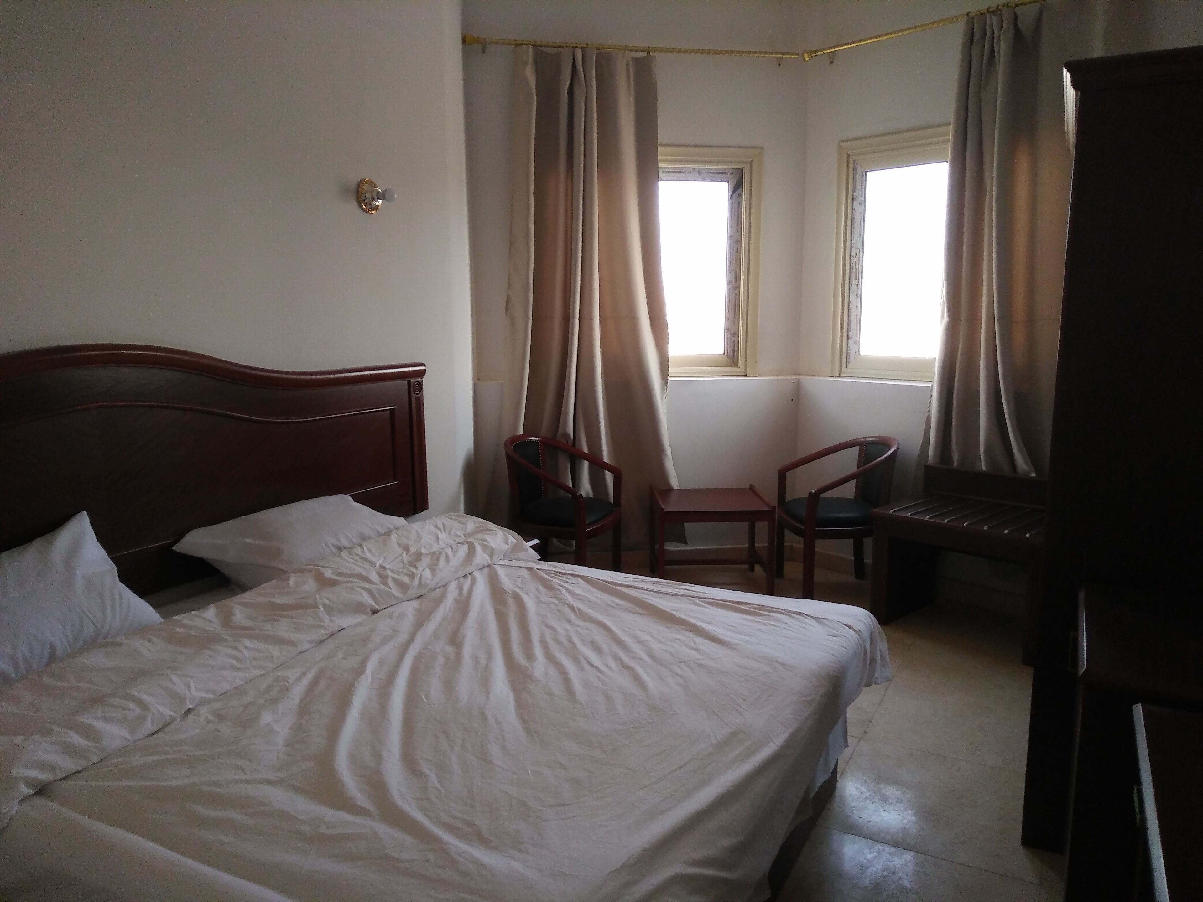 A hotel room with a wooden bed, two chairs, a desk, and a TV.