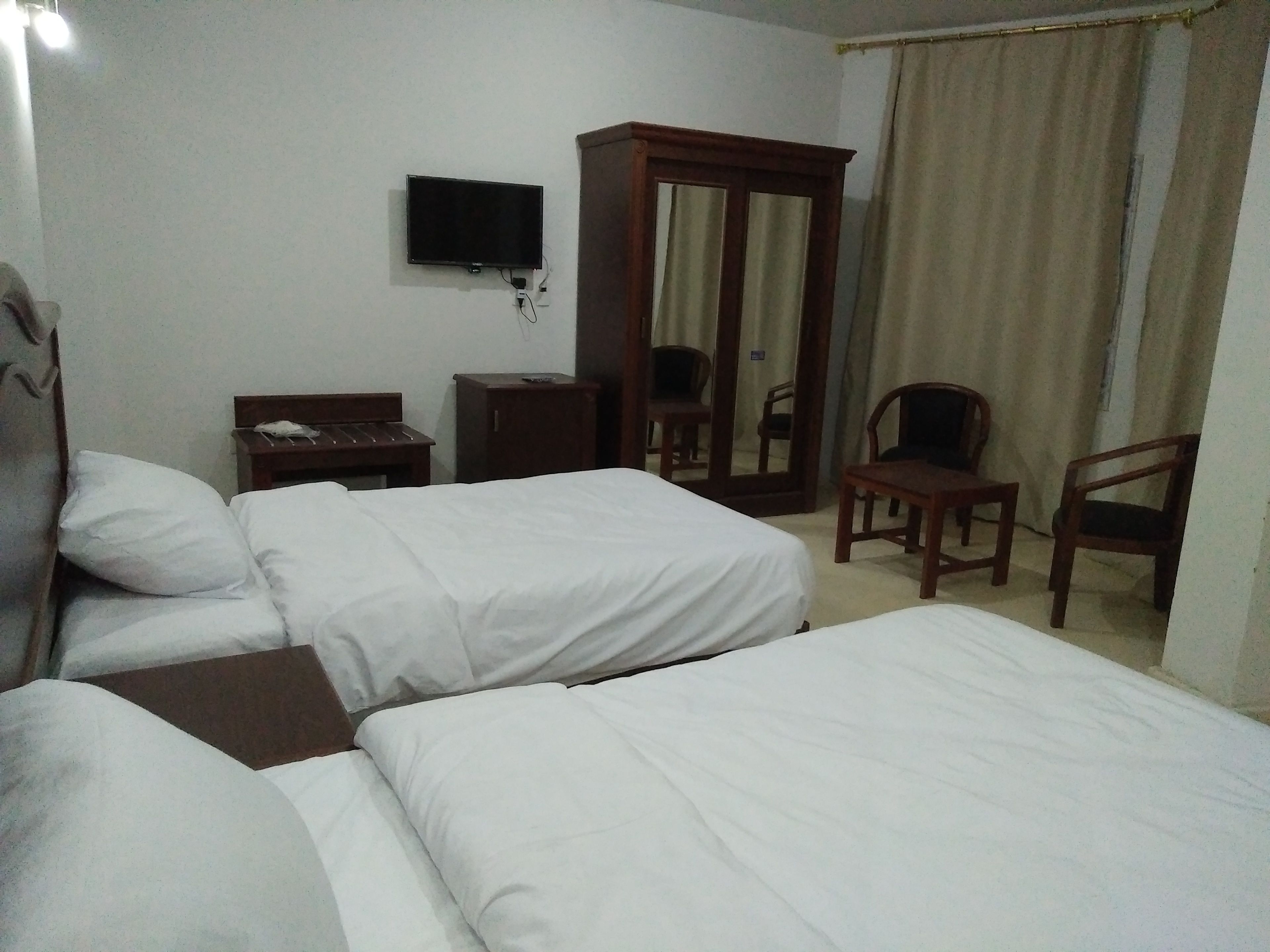 Habitación de hotel con dos camas, televisión, armario, escritorio y una silla.