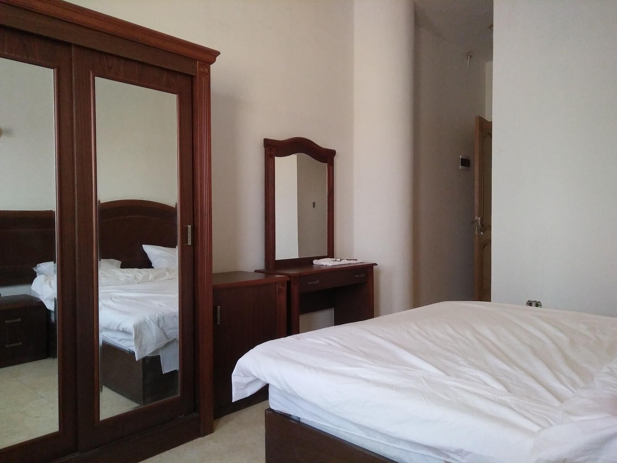 A bedroom with a bed, a wooden dresser, a mirror, and a wardrobe.