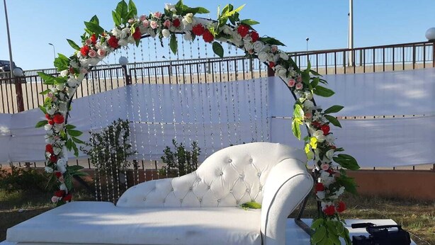 Um sofá branco sob um arco floral, com uma câmera e um controle remoto na mesa.