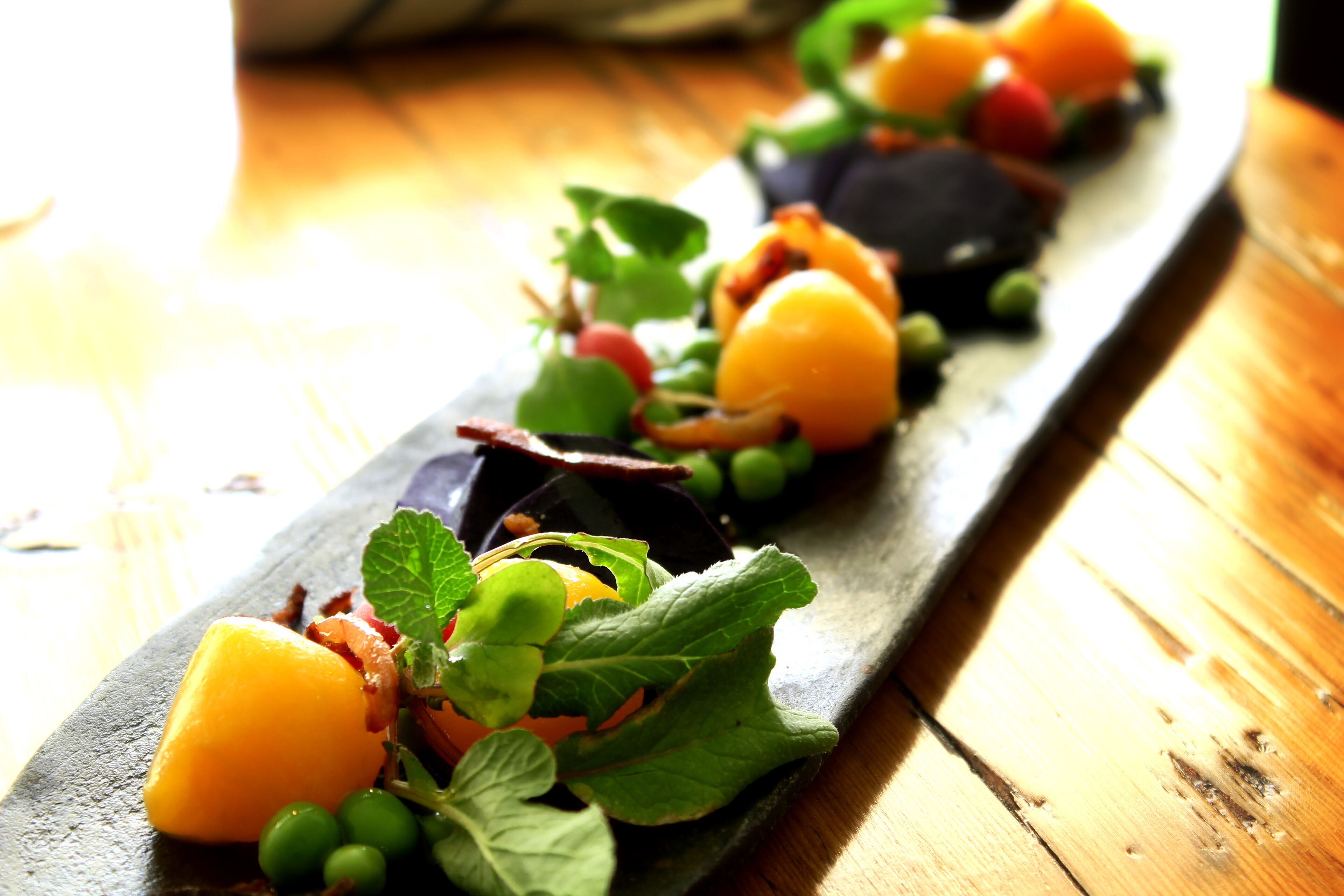 A wooden table with a long, narrow serving dish containing a variety of fresh fruits and vegetables.