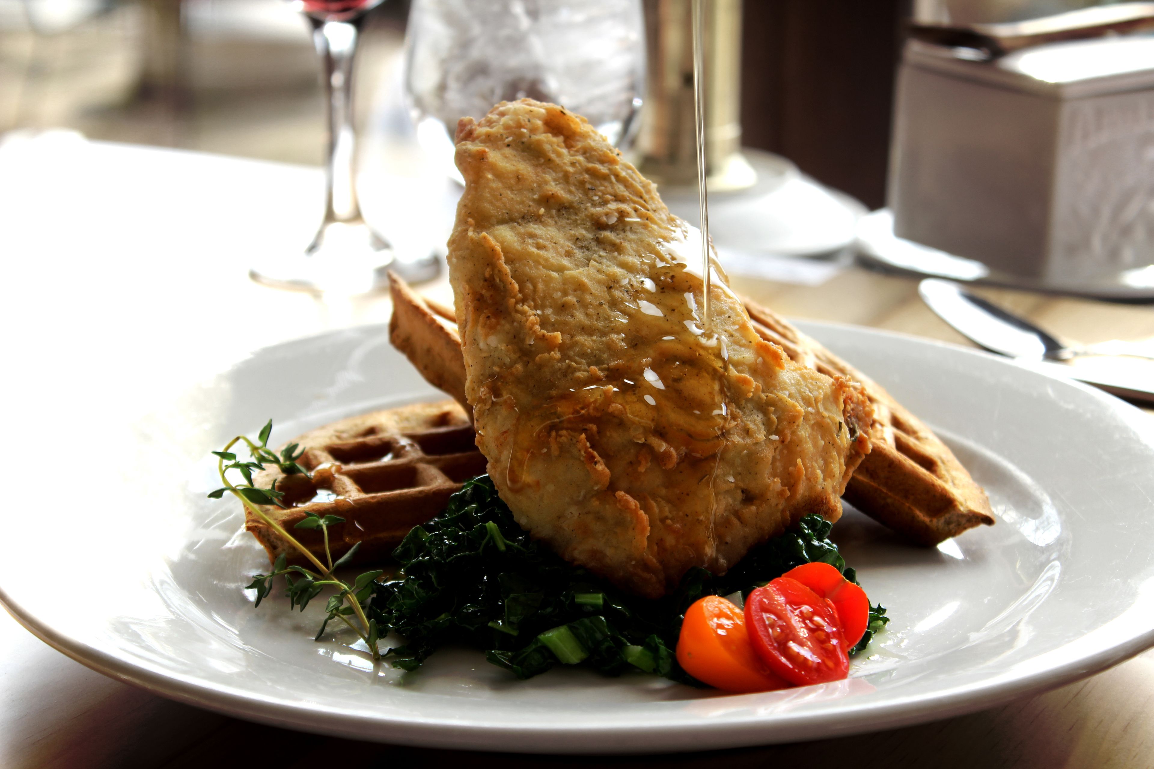 A plate with a piece of fried chicken, a waffle, and some greens.