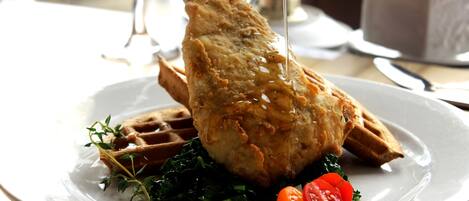 A plate with a piece of fried chicken, a waffle, and some greens.