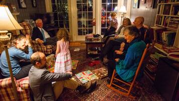 A group of people in a cozy living room with a fireplace, comfortable seating, and a bookshelf.