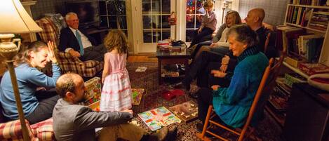 A group of people in a cozy living room with a fireplace, comfortable seating, and a bookshelf.