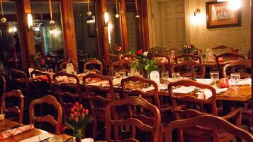 A restaurant with multiple wooden tables and chairs, each set with a candle, a vase with flowers, and a menu.