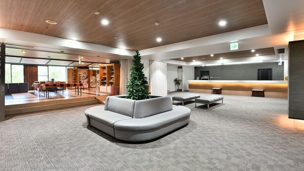 A spacious lobby with a reception desk, a seating area with a Christmas tree, and a large window providing natural light. - Shiga Grand Hotel (Yamanouchi)