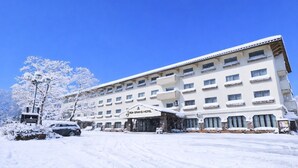 A large hotel with multiple floors and balconies, snow-covered surroundings, and a clear blue sky. - Shiga Grand Hotel (Yamanouchi)